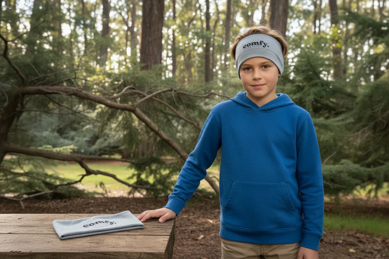 Child wearing a blue hoodie and headband with 'comfy' text, standing outdoors in a forest.